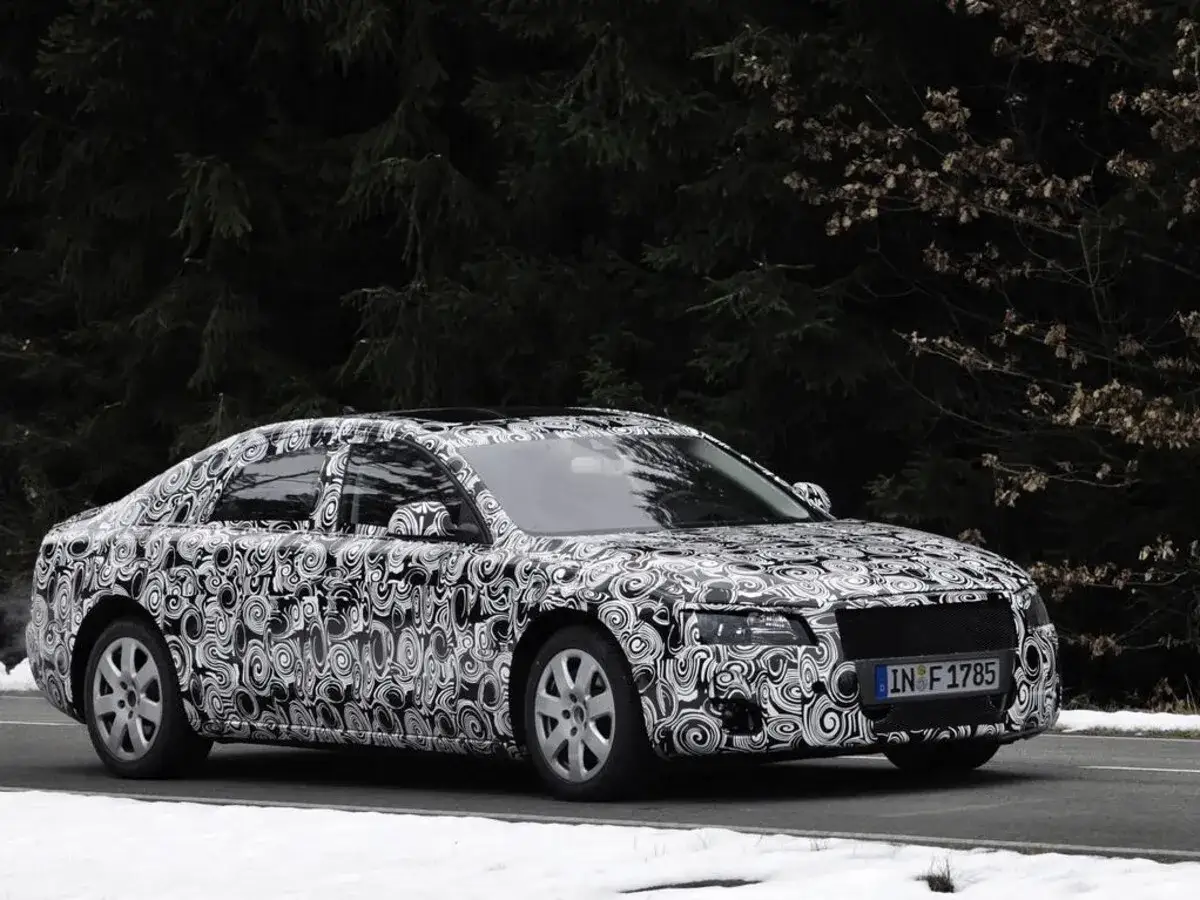 Audi Limousine mit Tarnfolie fährt auf schneebedeckter Straße vor dunklem Wald.