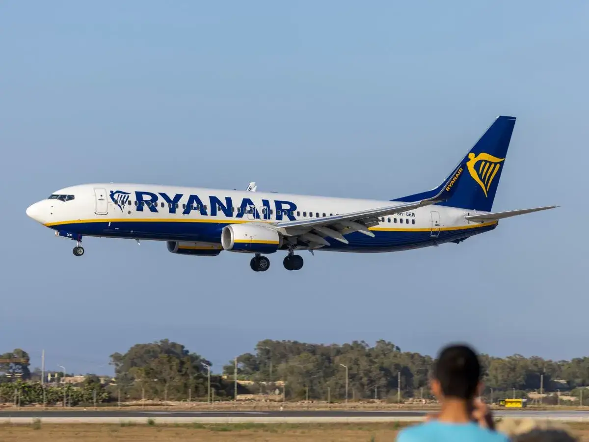 Samolot Ryanair lądujący na tle nieba i drzew.