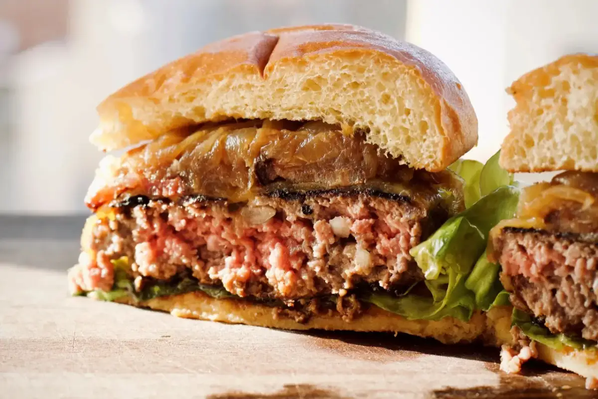 Przekrojony, soczysty burger z karmelizowaną cebulą i sałatą na desce.