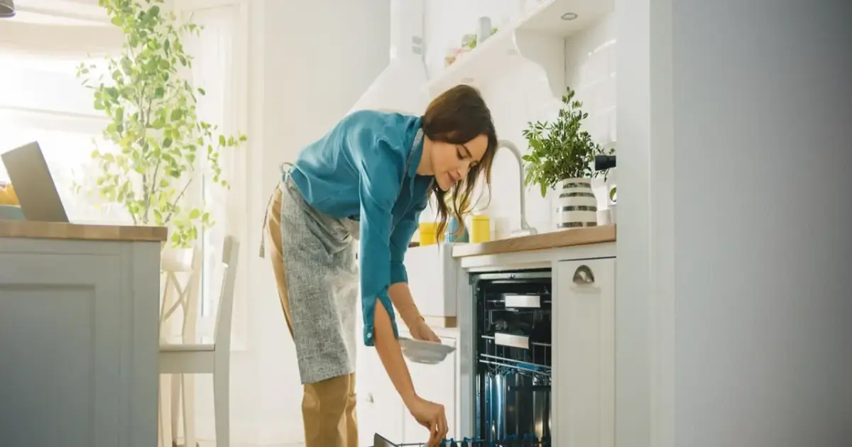 Kobieta wkłada talerz do zmywarki. Zastanawia się, czy lepsza będzie zmywarka 45 czy 60 cm.