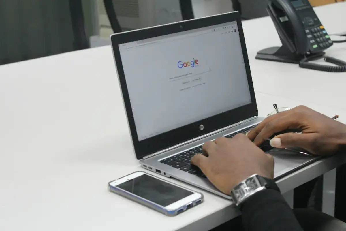 Dłonie piszące na laptopie z otwartą stroną Google, obok leży smartfon.