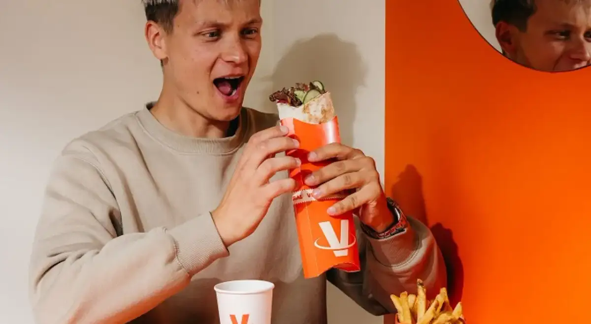Młody mężczyzna z zachwytem trzyma w rękach viral kebab. Jego mina sugeruje, że opinie o tym daniu są w pełni uzasadnione.