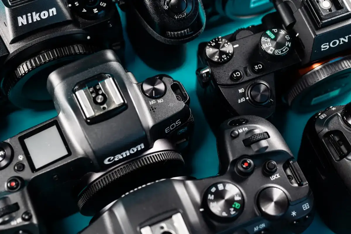 Zbliżenie na kilka aparatów cyfrowych marek Nikon, Canon i Sony ułożonych na niebieskim tle.