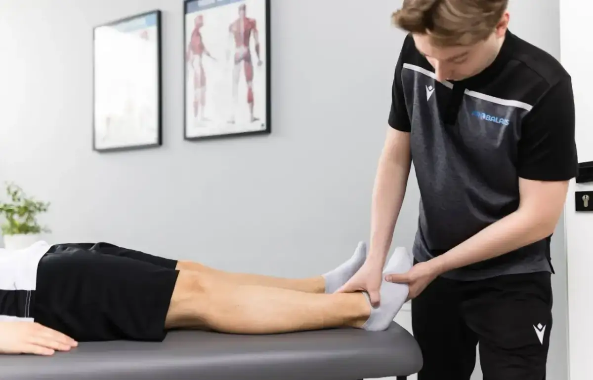 Fizjoterapeuta w sporcie delikatnie bada stopę zawodnika leżącego na kozetce.