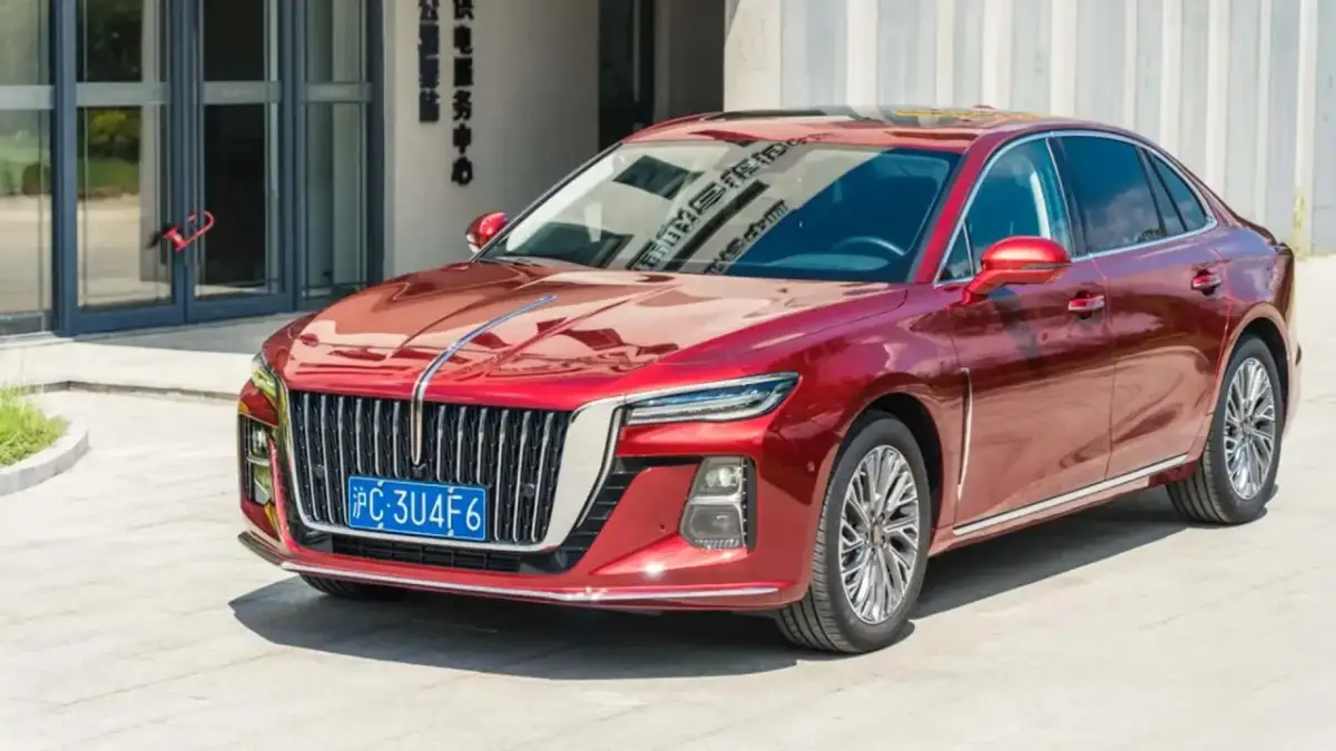 Elegancki, czerwony Hongqi H5 lśni w słońcu przed nowoczesnym budynkiem.