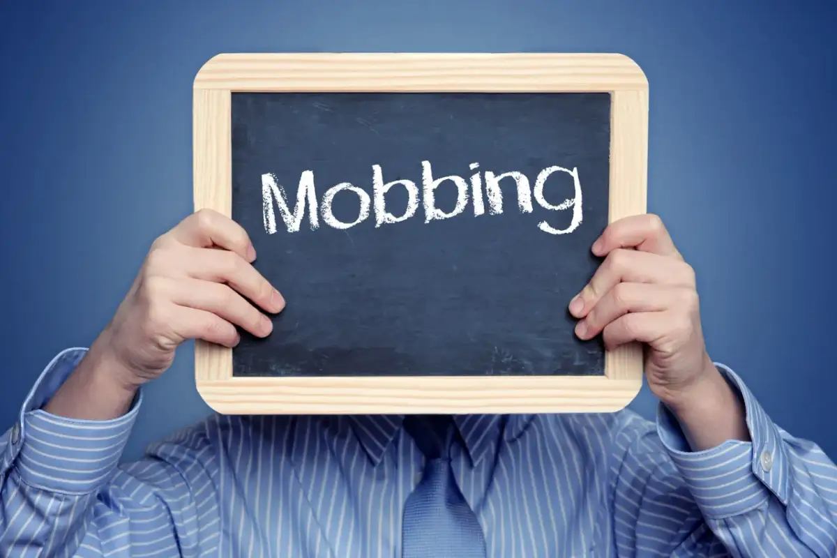 Osoba w koszuli trzyma tabliczkę z napisem "Mobbing". To symbol naruszenia dóbr osobistych i nękania w pracy.