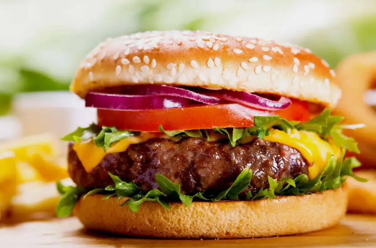 Soczysty burger z serem, pomidorem, czerwoną cebulą i sałatą na bułce z sezamem.