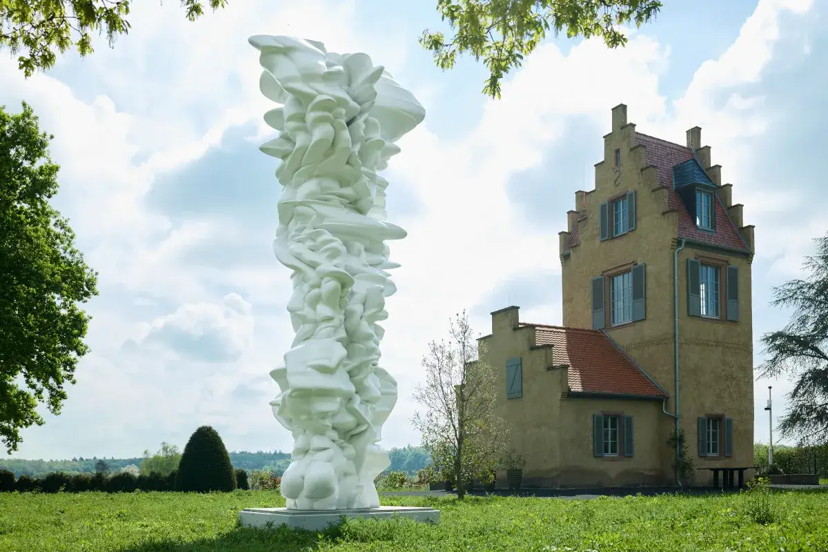 Weiße, organische Skulptur vor einem gelben Gebäude im Freien.