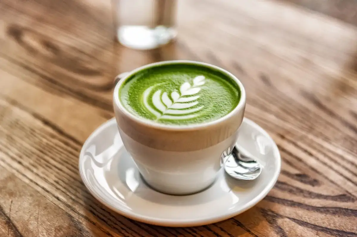 Zielone matcha latte z pianką i wzorem liścia na drewnianym stole.