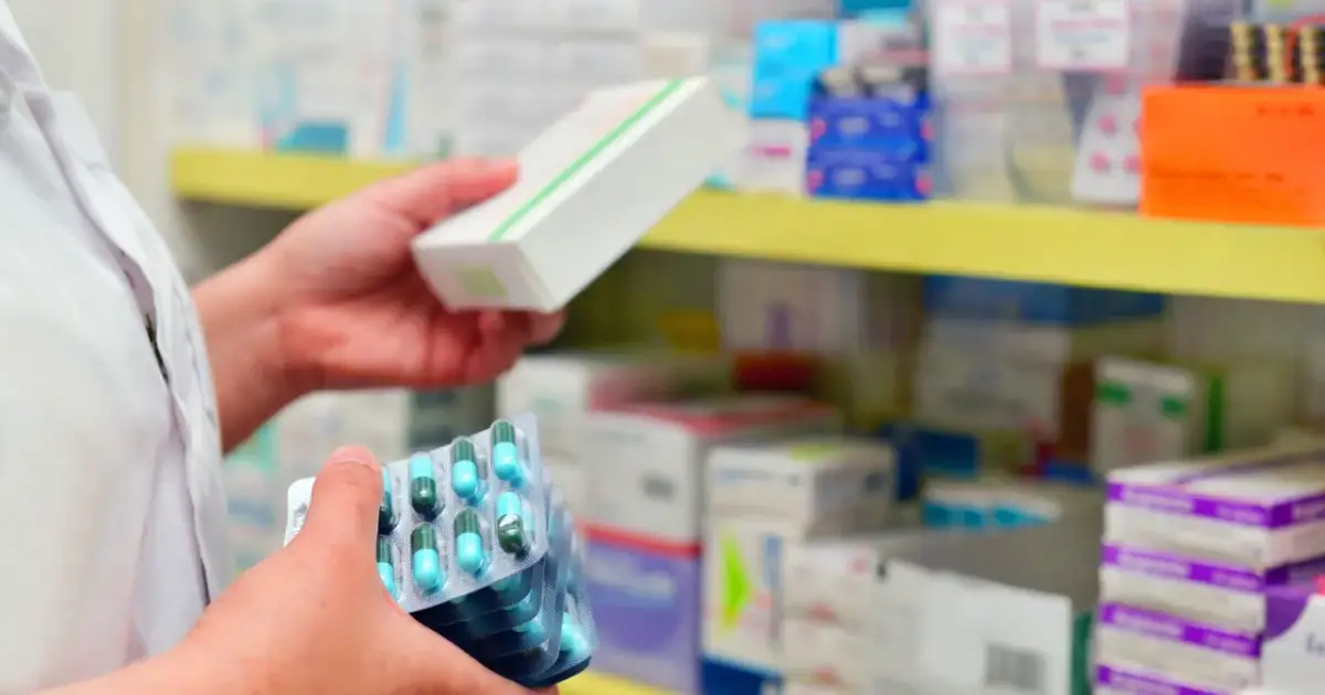 Farmaceuta trzyma opakowanie leku i kilka blistrów kapsułek. Pokazuje, ile ważna jest recepta i prawidłowe dawkowanie.