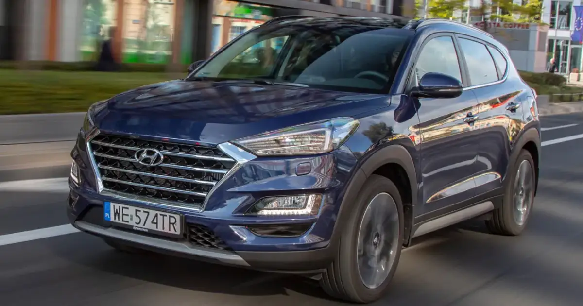 Ciemnoniebieski Hyundai Tucson 2025 w ruchu miejskim, z widocznym grillem i reflektorami.