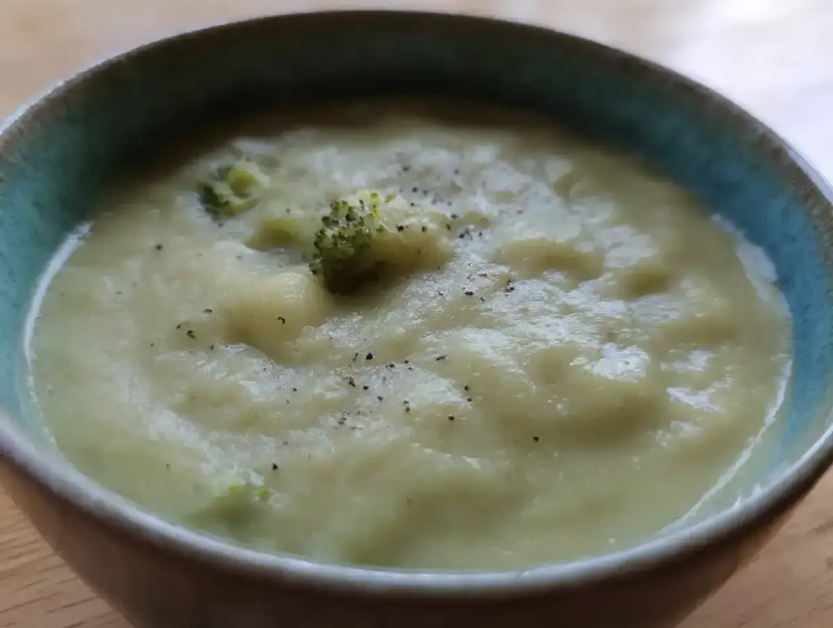 En krämig potatis och broccolisoppa, toppad med lite svartpeppar, serveras i en blå kantad skål.