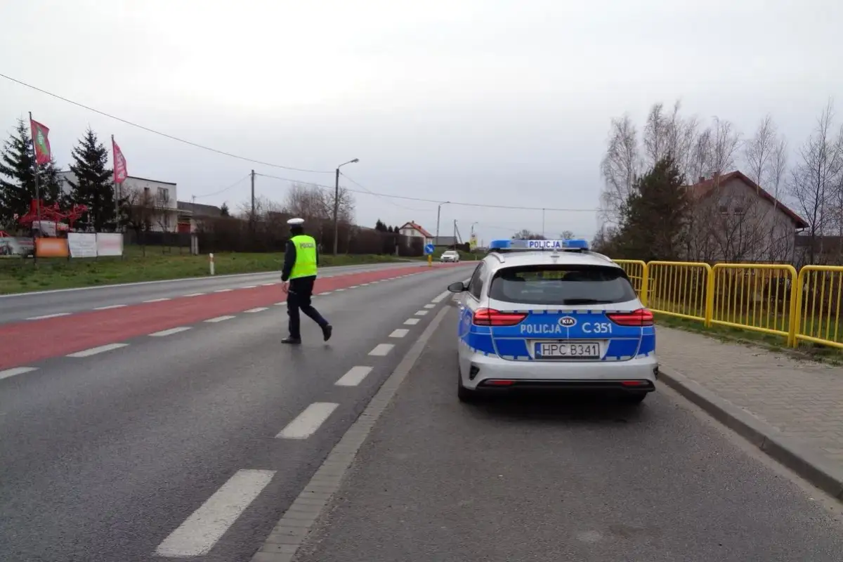 Policjant w kamizelce odblaskowej kieruje ruchem obok radiowozu. Może to być kontrola drogowa lub reakcja na wykroczenie 97 kw.