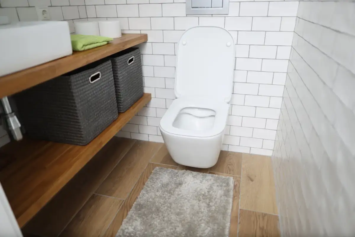 Nowoczesna łazienka z podwieszanym WC. Obok półka z koszami, ręcznikiem i papierem toaletowym. Widać, ile miejsca na wc podwieszane zajmuje.