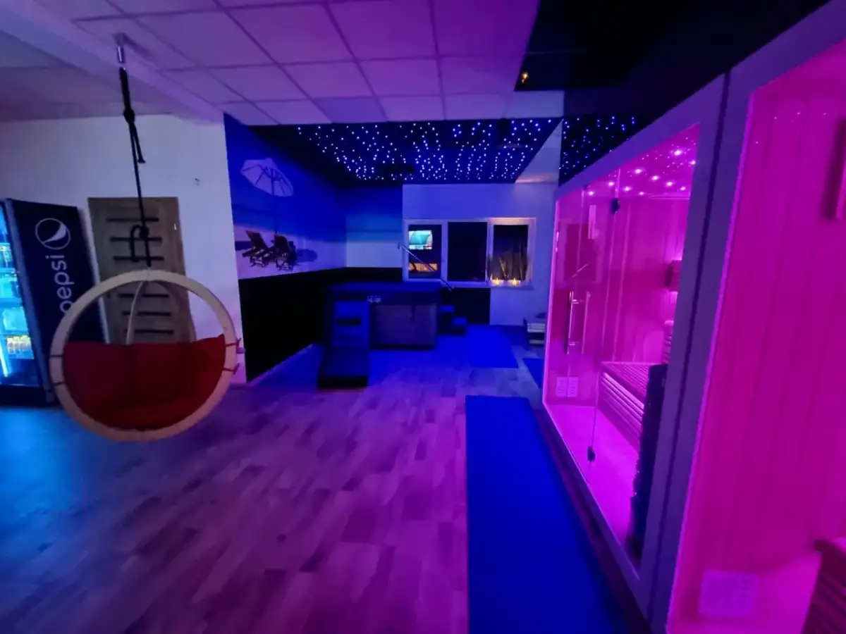 Nowoczesne spa z sauną, jacuzzi i wiszącym fotelem, oświetlone neonowym światłem.