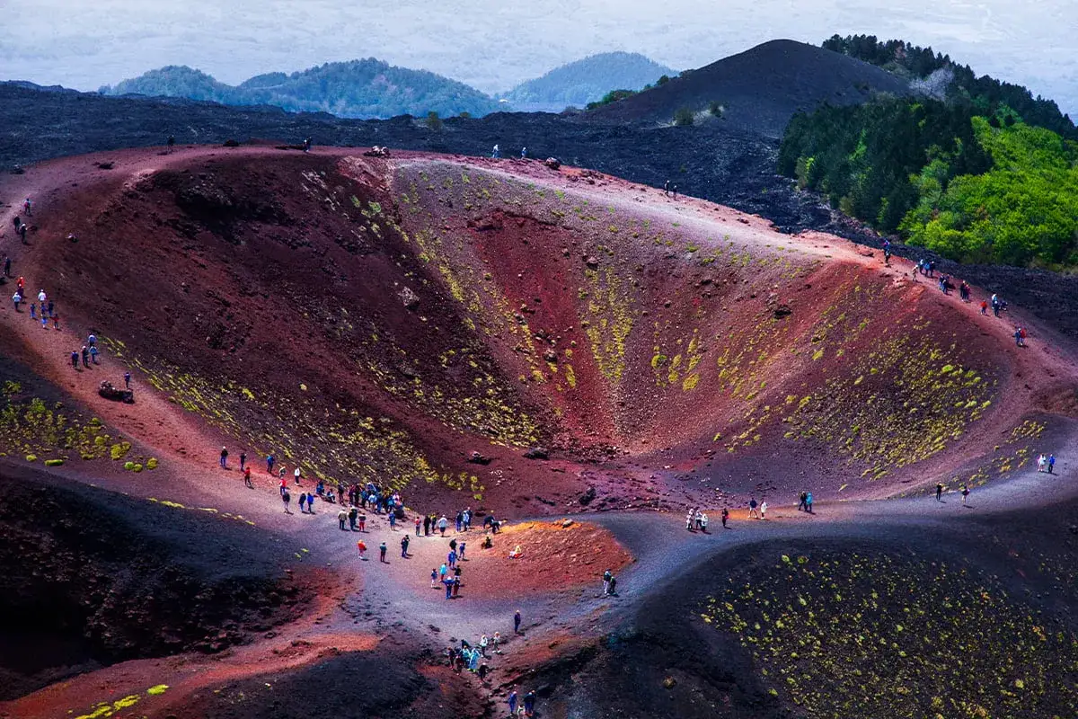 Grupa turystów wędruje po kraterze wulkanu Etna, podziwiając jego czerwoną i czarną, wulkaniczną ziemię porośniętą mchem.