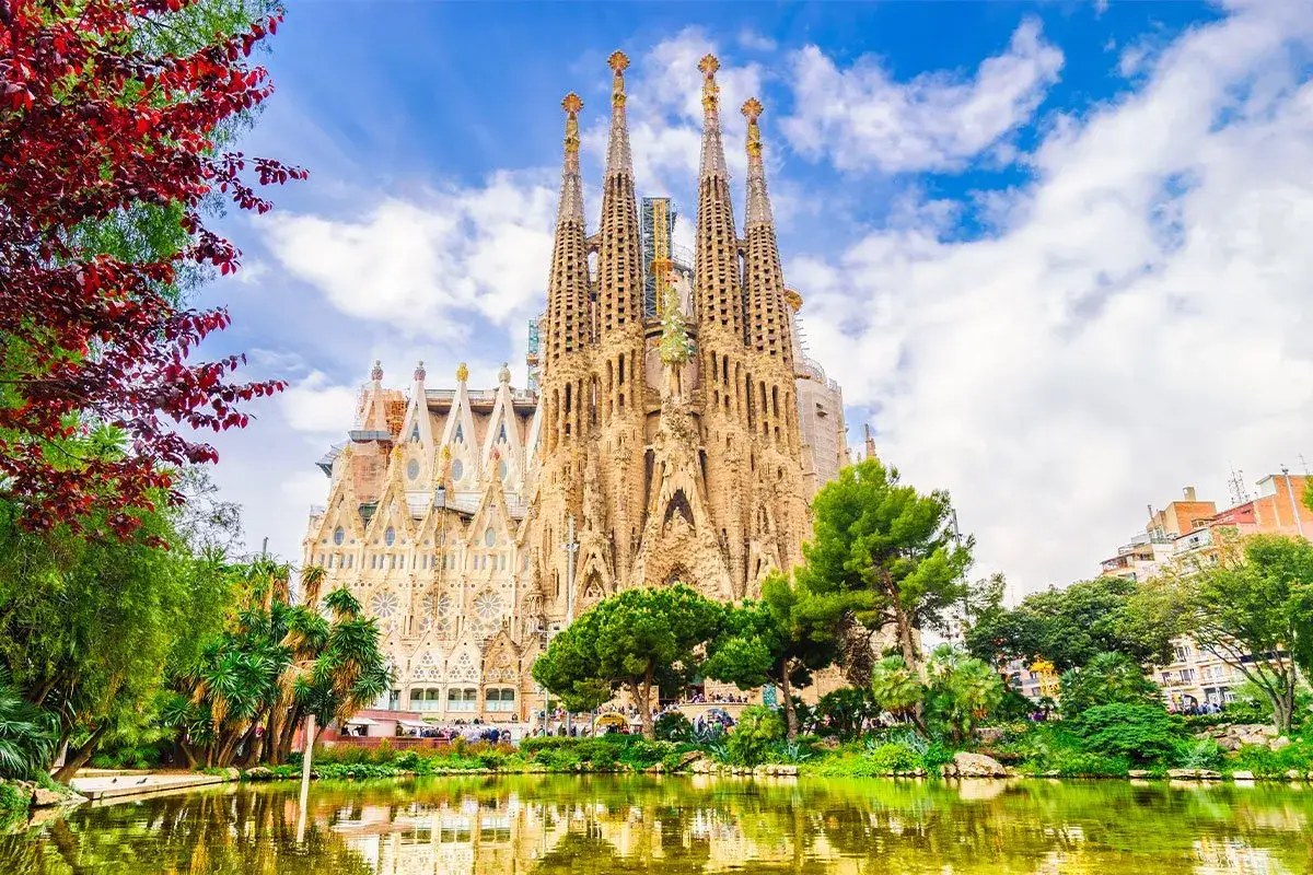 Sagrada Familia, z jej unikalną architekturą i otaczającą zielenią, to miejsce pełne ciekawostek. Woda w stawie odbija majestatyczne wieże.