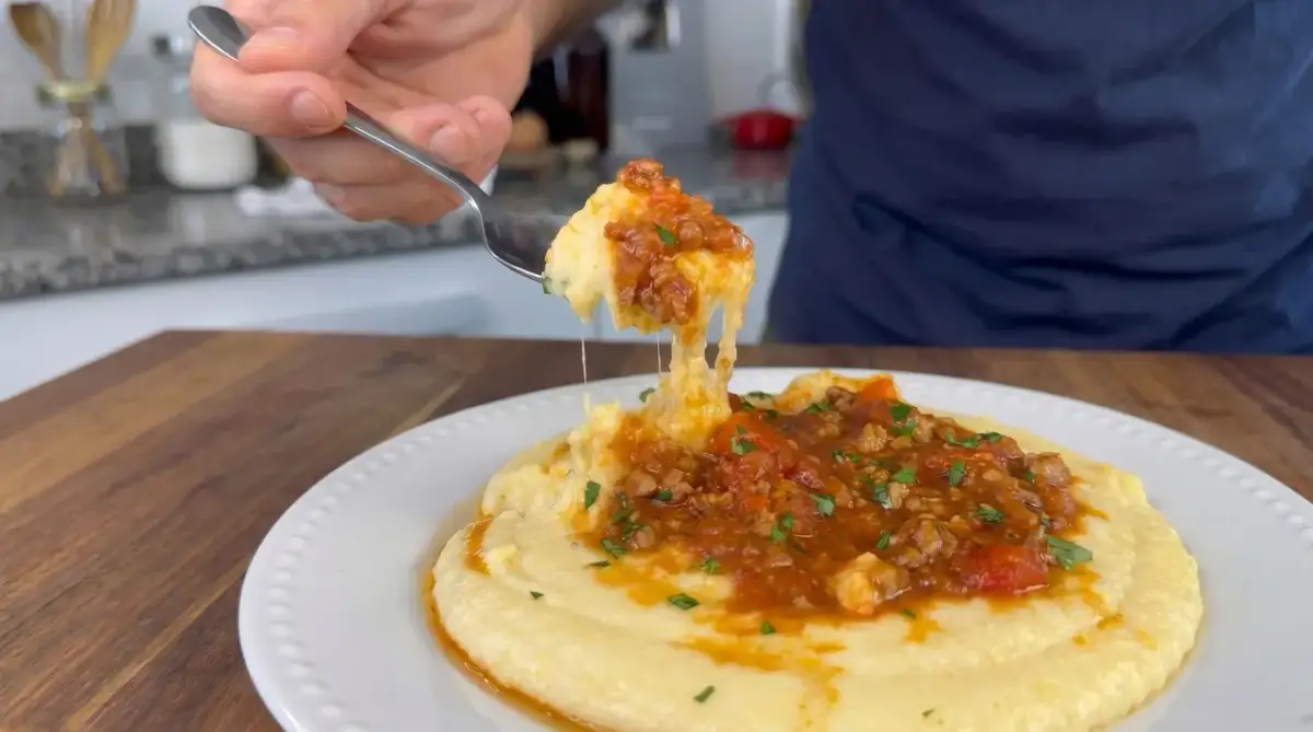 Un tenedor levanta una porción de polenta con tuco, mostrando su textura cremosa y la rica salsa de carne y tomate.