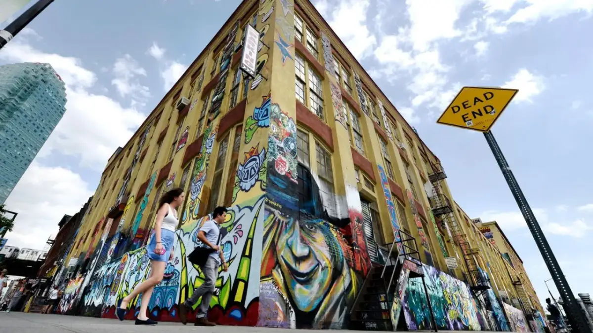 Gelbes Gebäude mit Graffiti-Kunst, Menschen gehen vorbei, "DEAD END"-Schild.