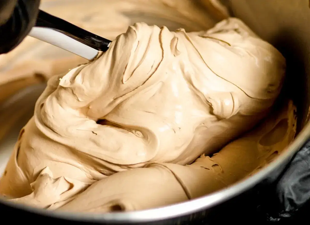 Gładka, kremowa masa o kolorze **salted caramel** jest mieszana łopatką w metalowej misce.