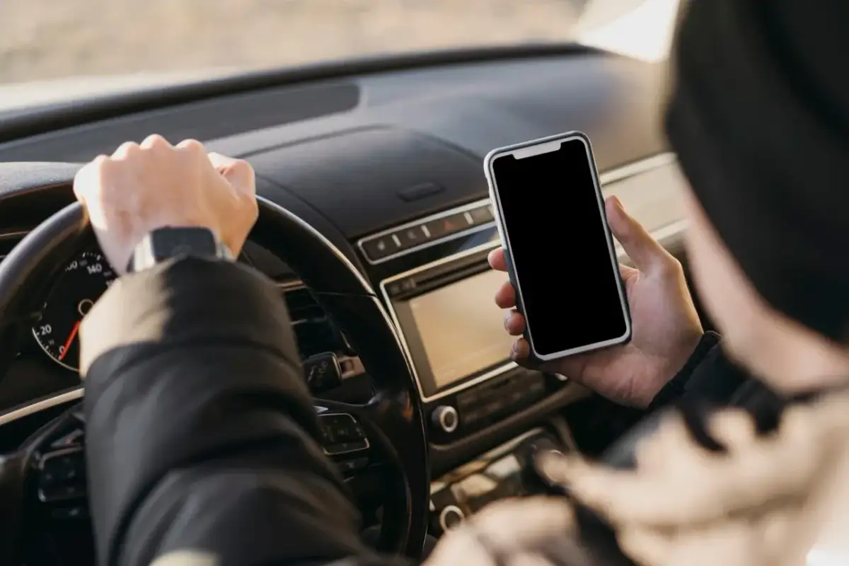 Kierowca trzyma telefon podczas jazdy, ryzykując mandat za korzystanie z telefonu.
