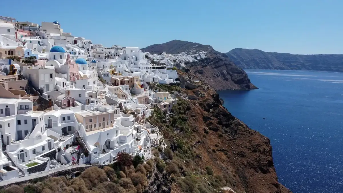 Białe domy Santorini na klifie, z błękitnymi kopułami kościołów, nad lazurowym morzem. Krajobraz jak po trzęsieniu ziemi, ale pełen życia.