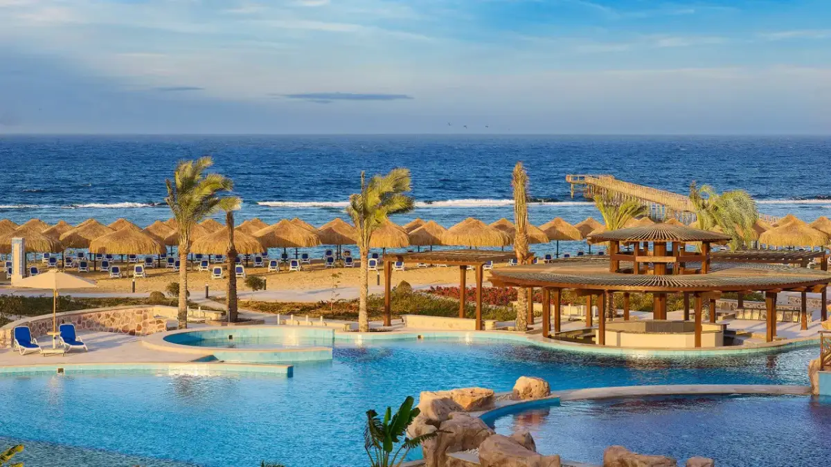 Relaks przy basenie i plaży z parasolami w hotelu Lazuli Marsa Alam. Błękitne morze i palmy tworzą rajski widok.