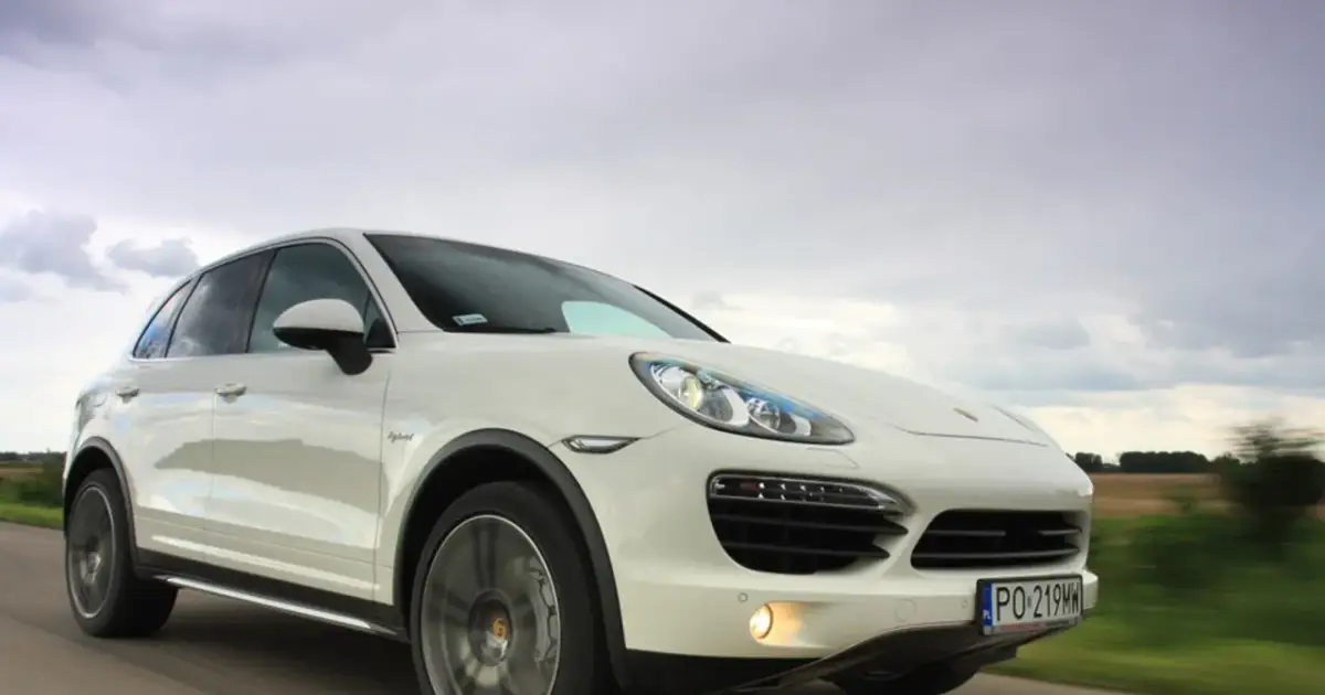 Biały Porsche Cayenne 2025 pędzi po drodze, chmury na niebie sugerują dynamiczną podróż.