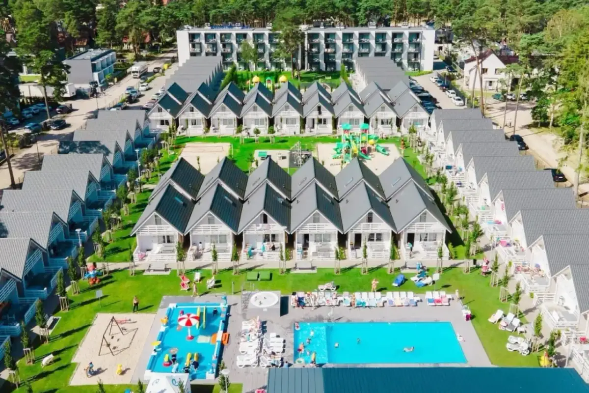 Widok z lotu ptaka na holiday park Kołobrzeg: rzędy białych domków z szarymi dachami, baseny, plac zabaw i zielone tereny.