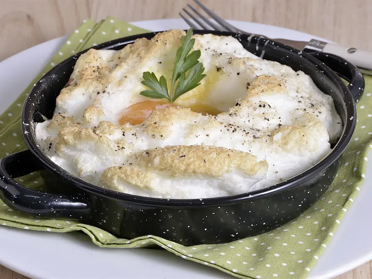 Delicioso huevo al horno, con clara montada y yema cremosa, adornado con perejil y pimienta.