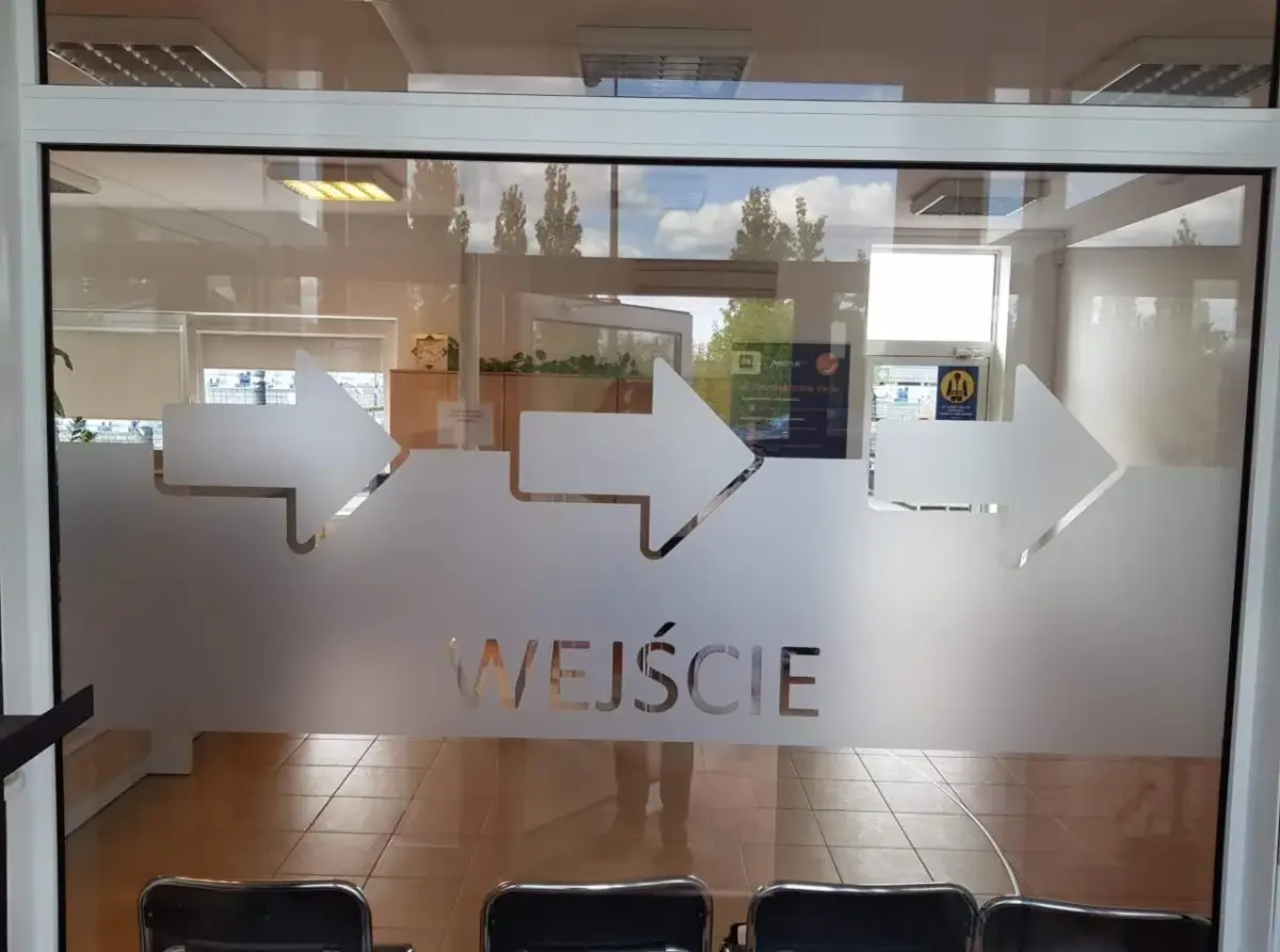 Szklane drzwi z matowymi strzałkami i napisem "WEJŚCIE".