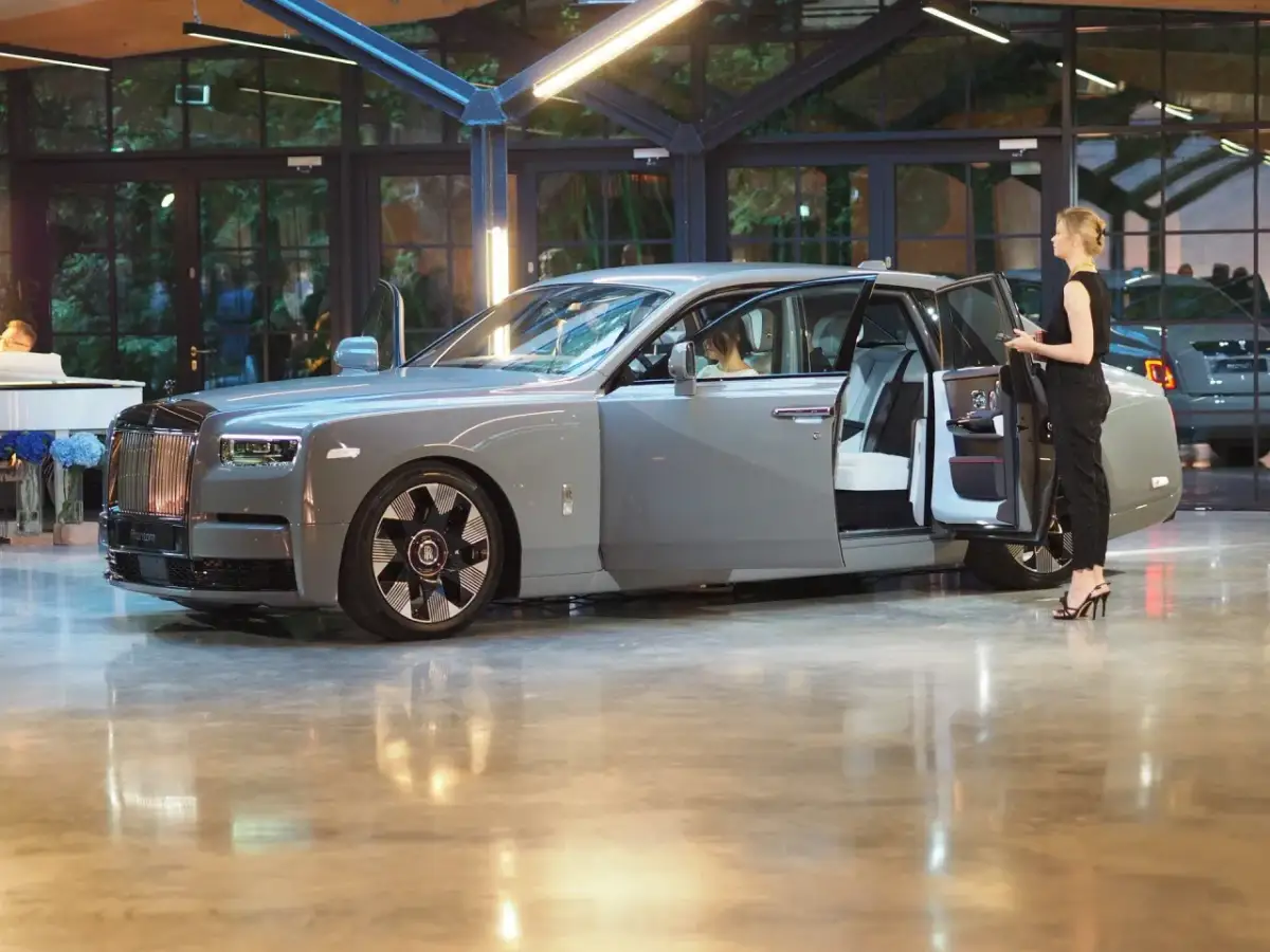 Elegancki szary Rolls-Royce Phantom z otwartymi drzwiami, obok którego stoi kobieta. Poznaj jego wyjątkową rolls royce phantom cena.