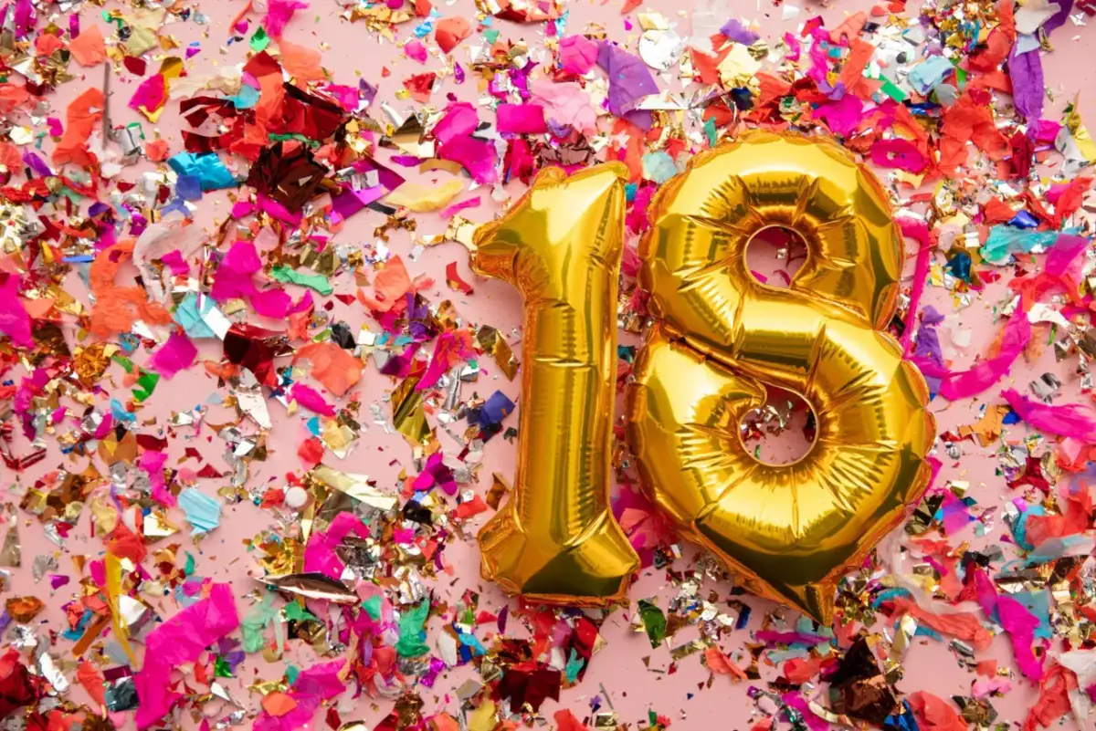 Złote balony z cyfrą 18 na tle kolorowych konfetti.
