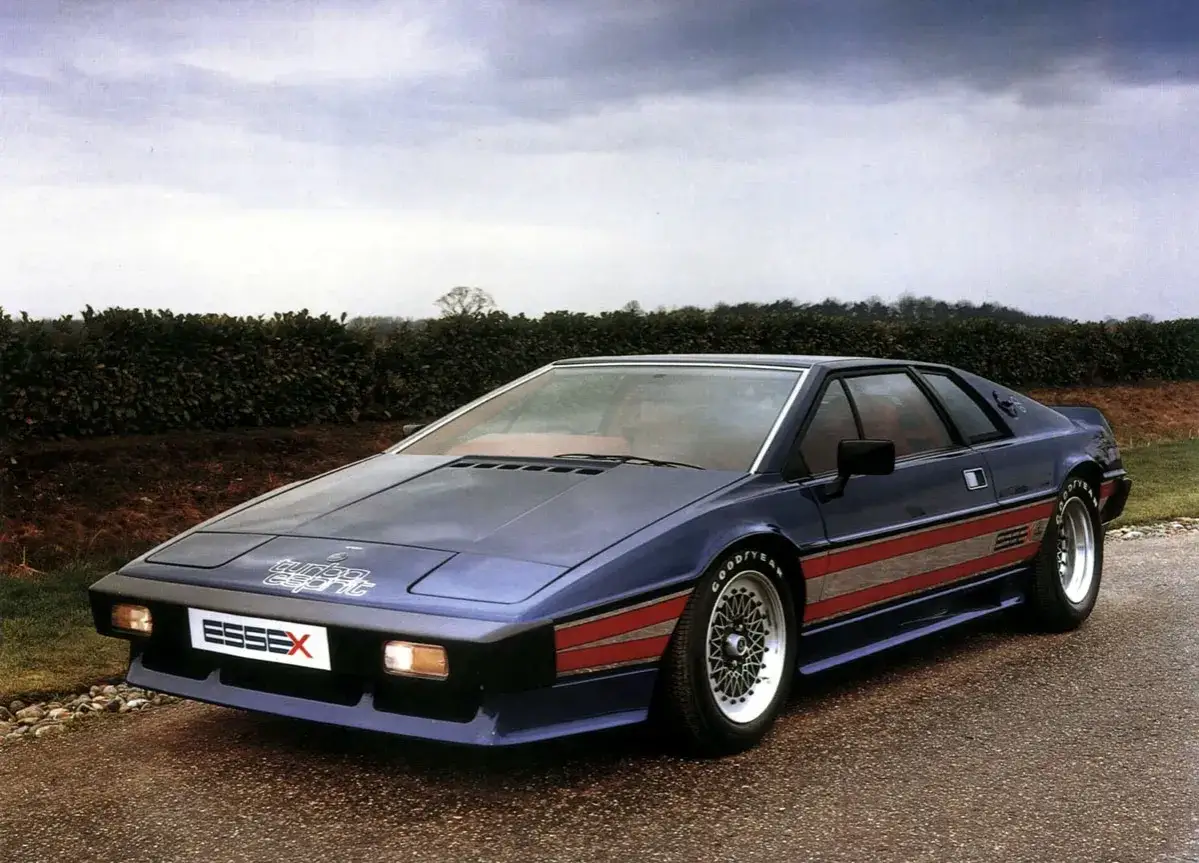 Niebieski Lotus Esprit Turbo Essex z czerwonymi pasami na boku, zaparkowany na drodze.