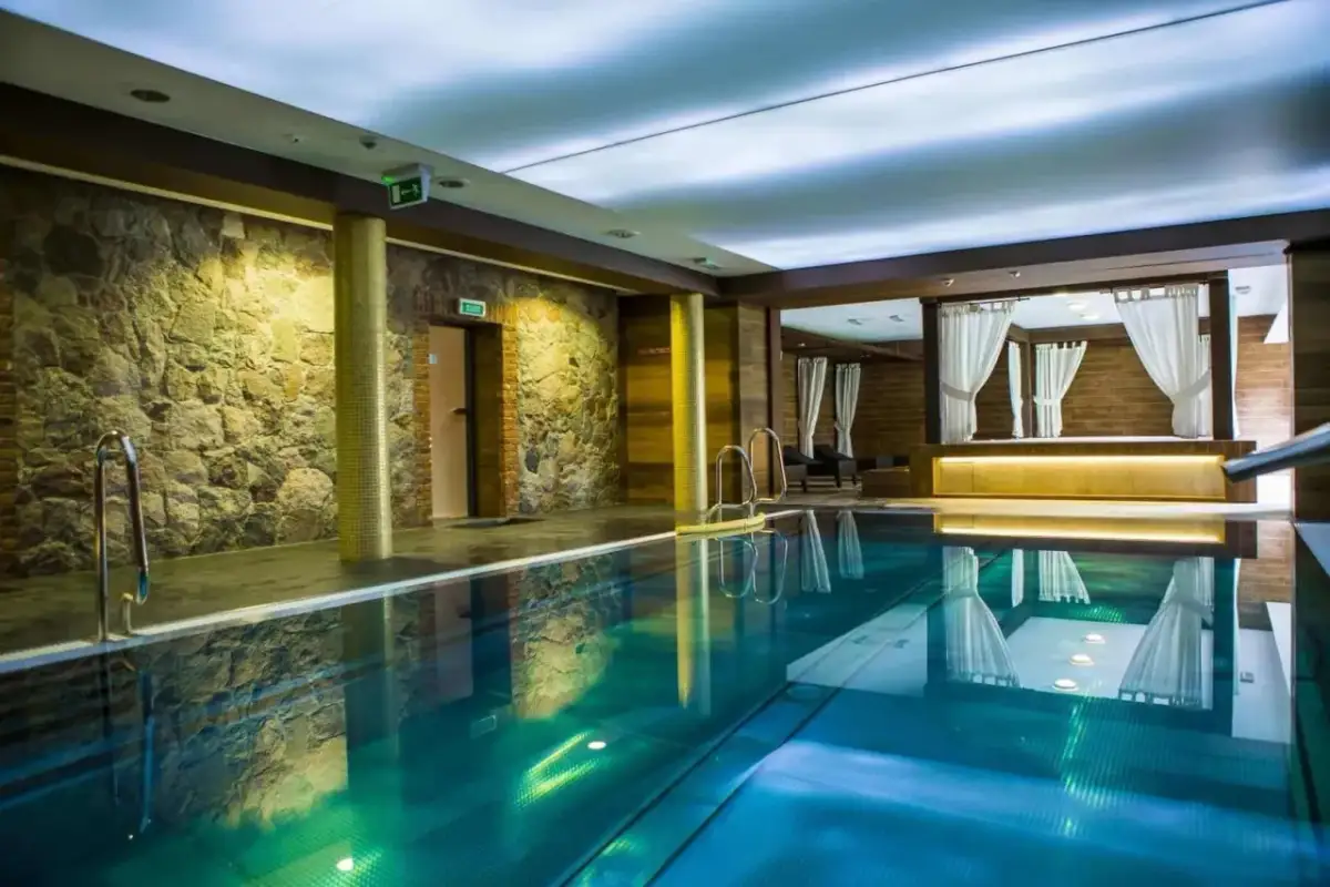 Basen w hotelu Aubrecht Country Spa Resort Koprzywnica. Woda w basenie ma piękny, turkusowy kolor, a ściany zdobi kamień i drewno.