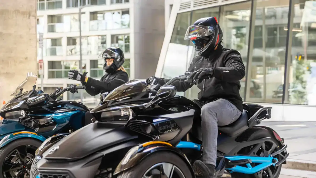 Para motocyklistów w kaskach i kurtkach na pojazdach Can-Am na tle miejskim.