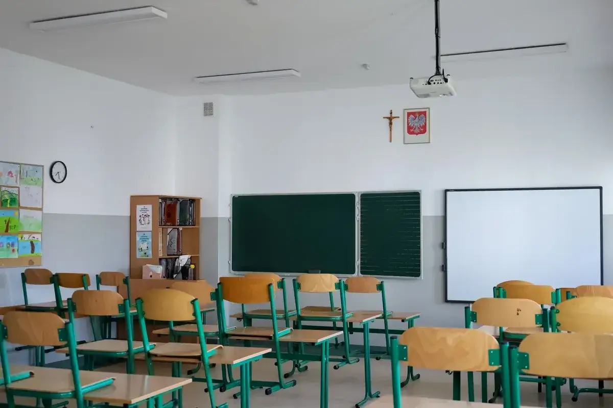 Pusta sala lekcyjna z ławkami, tablicą i projektorem.