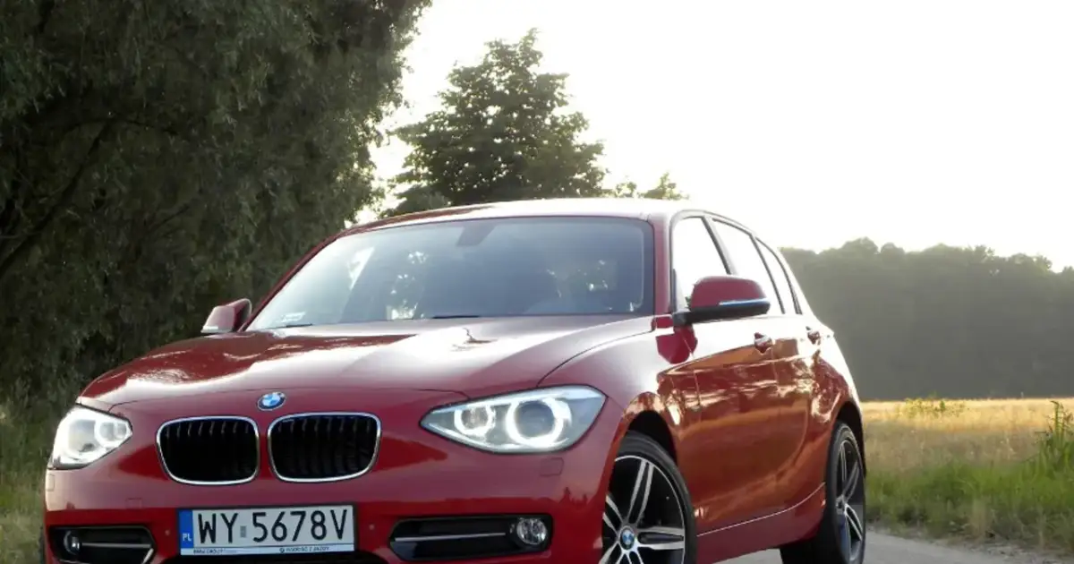 Czerwone BMW 118d na tle drzew i pól.