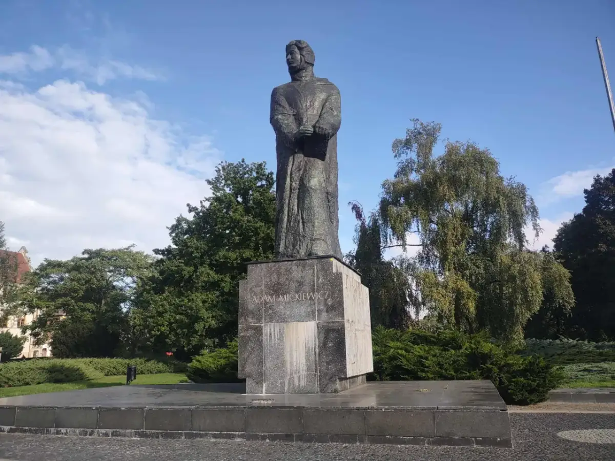 Pomnik Adama Mickiewicza na tle błękitnego nieba i zieleni.