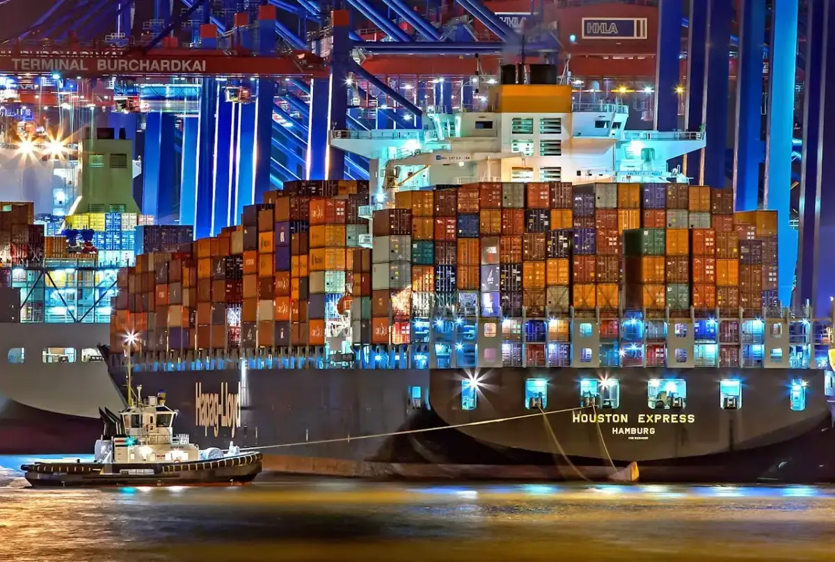 Kontenerowiec "Houston Express" z Hamburgu z ładunkiem kontenerów w porcie nocą, holowany przez statek.