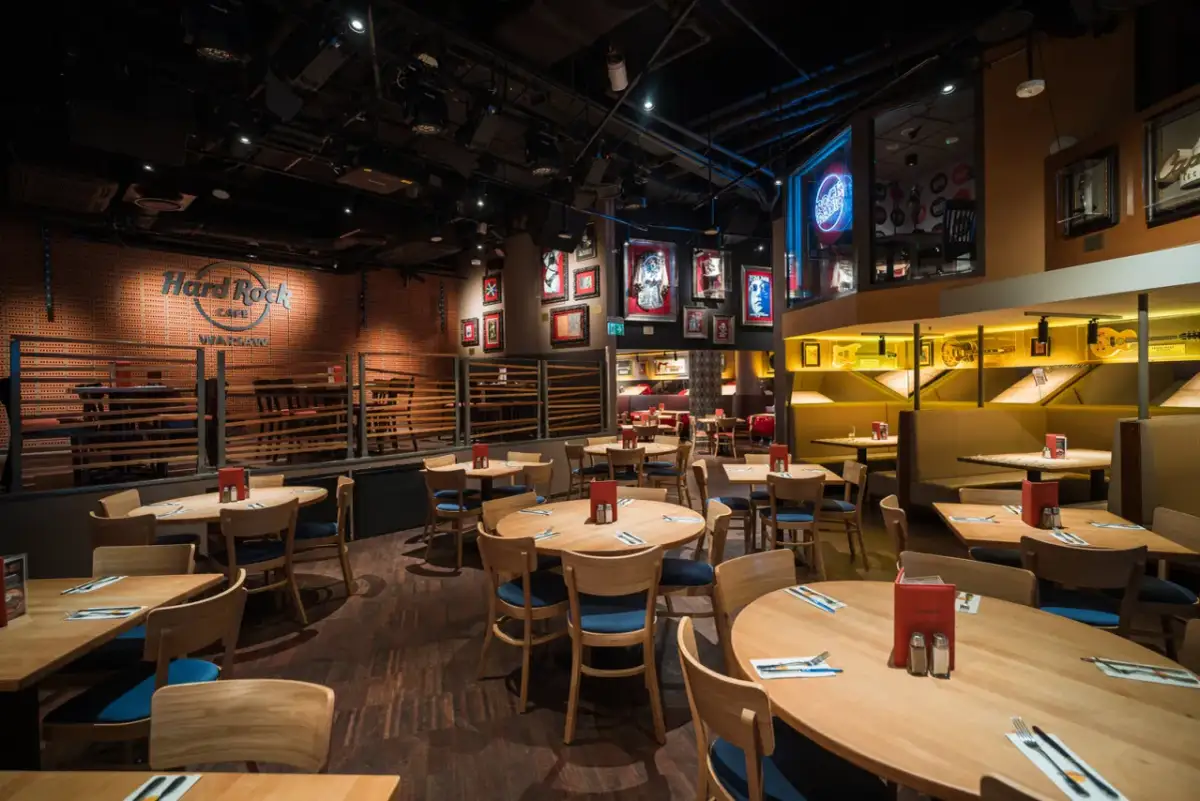 Wnętrze Hard Rock Cafe Warszawa. Drewniane stoły i krzesła, ściany ozdobione pamiątkami muzycznymi i neonem "Rock Radio".