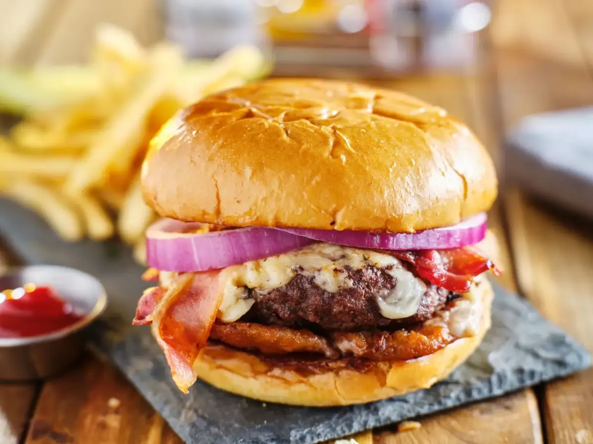 Soczysty burger z bekonem, serem i czerwoną cebulą, podany z frytkami i ketchupem.