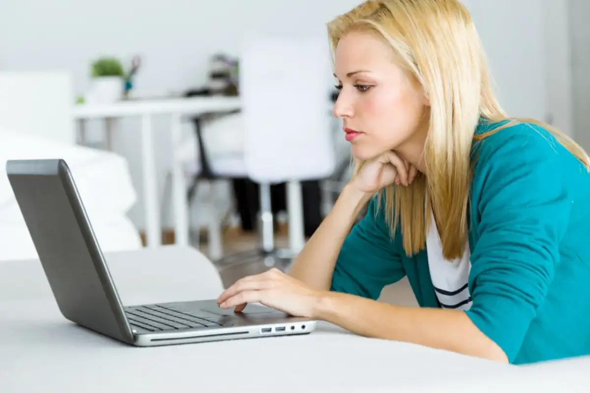 Kobieta z blond włosami pracuje na laptopie, analizując dokumenty dotyczące spłaconego komornika i kredytu hipotecznego.
