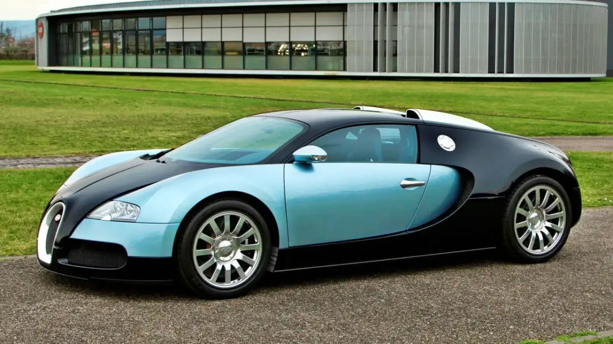 Błękitno-czarny Bugatti Veyron na tle nowoczesnego budynku i zielonego trawnika.