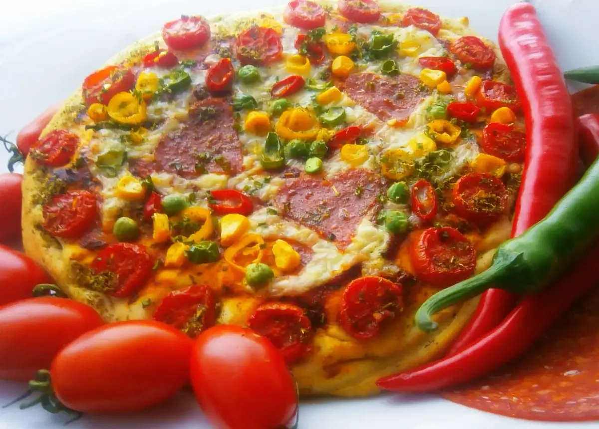 Pyszna pizza pepperoni z pomidorkami, papryką i zielonym groszkiem, otoczona świeżymi papryczkami chili i pomidorami.