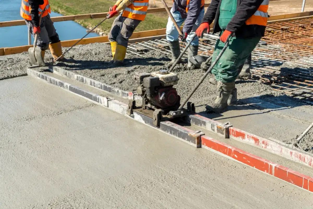 Budowlańcy używają wibrołaty do wyrównania świeżego betonu na budowie.