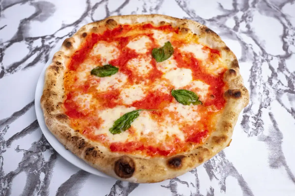 Pyszna pizza napoletana z pomidorami, mozzarellą i bazylią na białym talerzu, na tle marmurowego wzoru.
