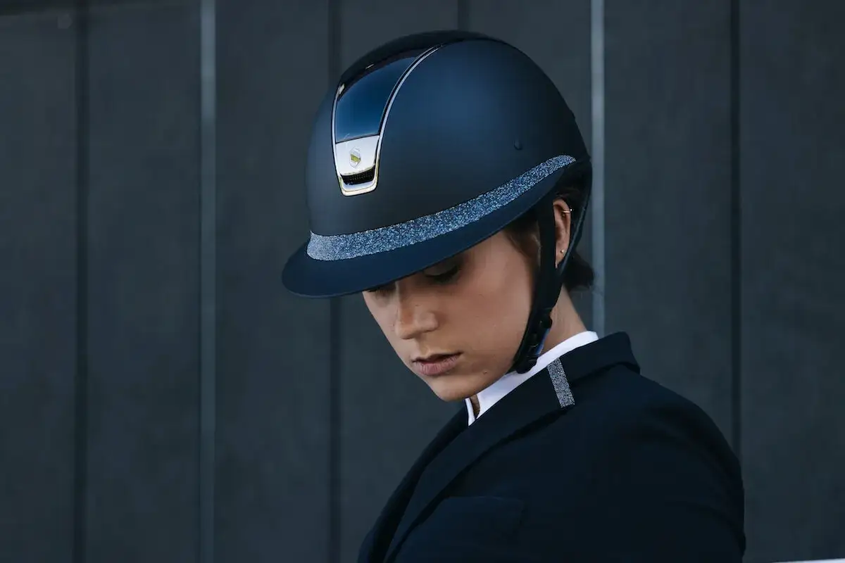 Elegancki kask marki kask, ozdobiony brokatową taśmą, noszony przez kobietę w czarnym żakiecie.
