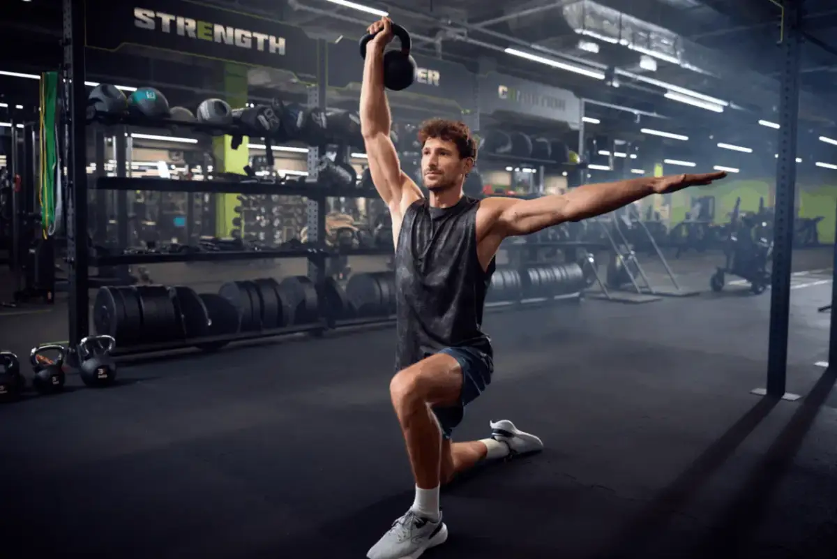 Mężczyzna w siłowni wykonuje ćwiczenie z kettlebell. To tbc co to za ćwiczenie, ale wygląda na skuteczne.