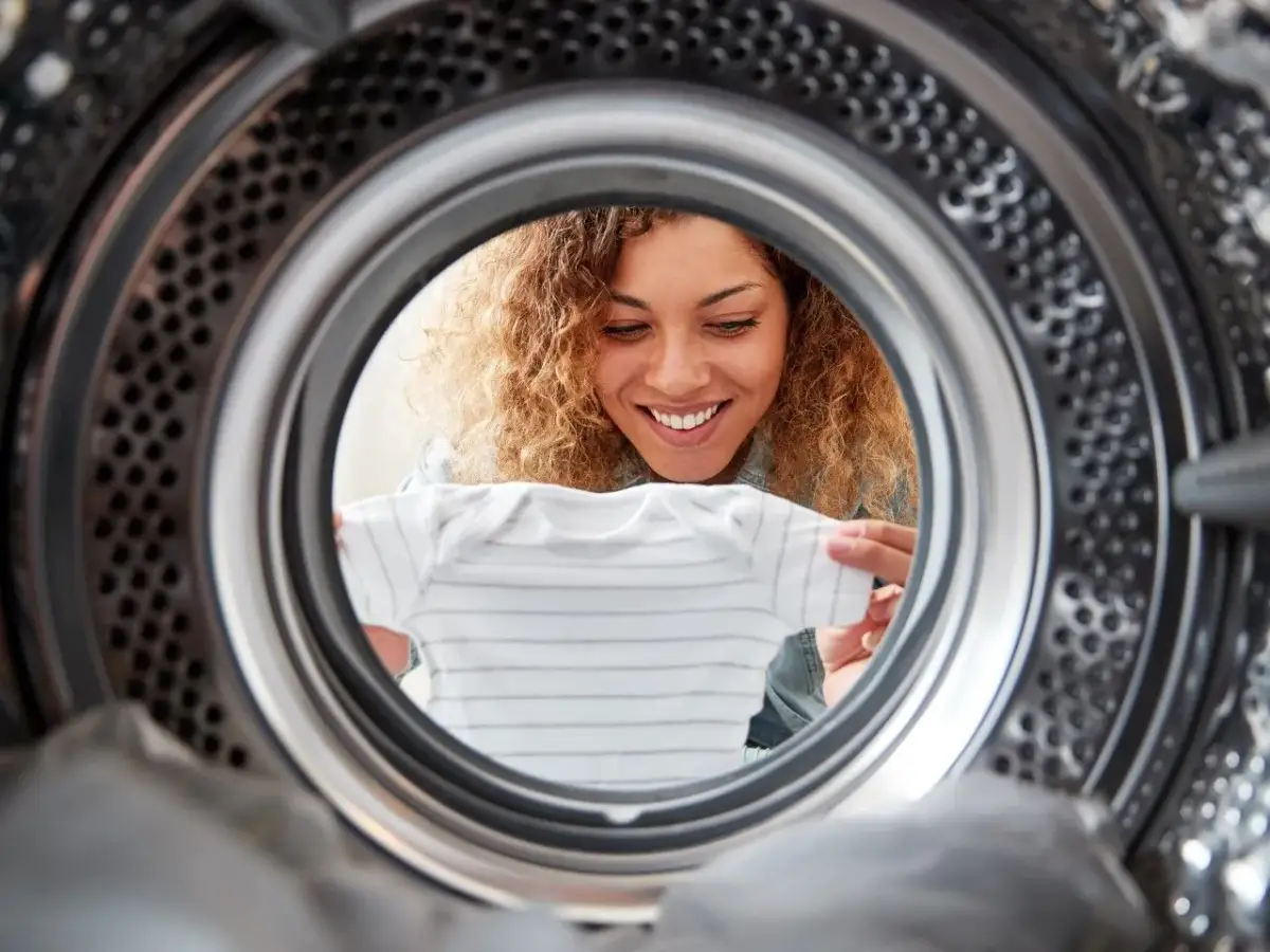 Uśmiechnięta kobieta wkłada ubranko do suszarki bębnowej Whirlpool.